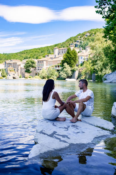 Couple au bord de l'eau devant un village d'Ardèche