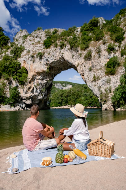 Couple pique-niquant au bord de l'Ardèche avec le Pont d'Arc en fond